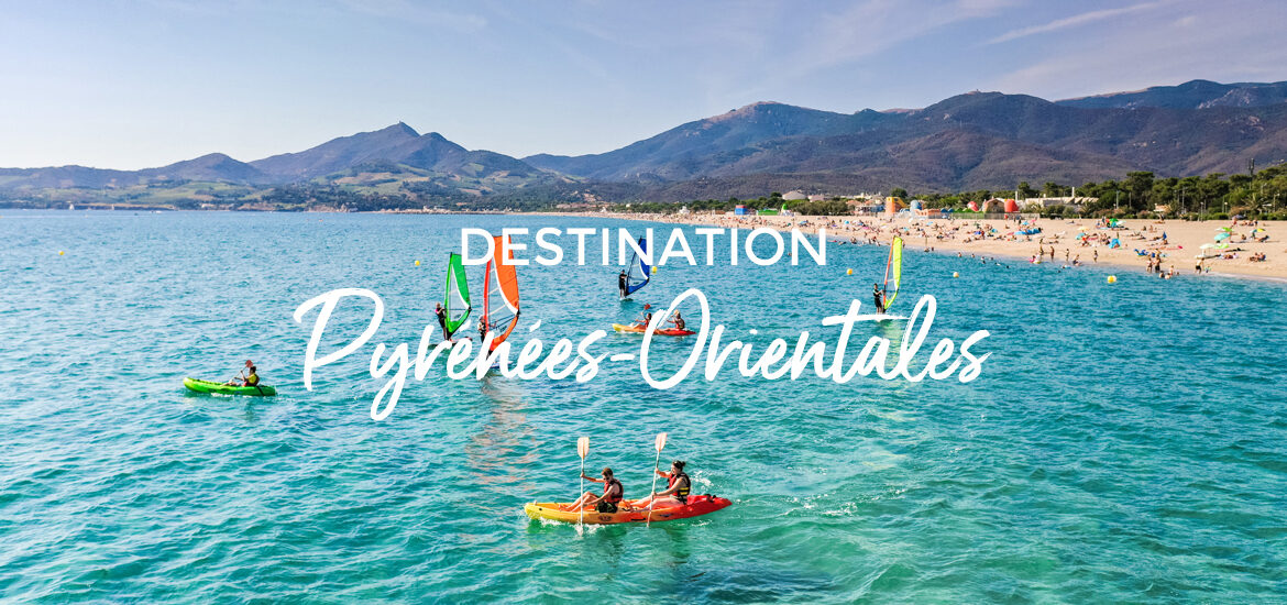 Plage animée des Pyrénées-Orientales avec des planches à voile et des kayakistes sur l'eau, et des montagnes en arrière-plan. Le texte "Destination Pyrénées-Orientales" est superposé sur l'image.