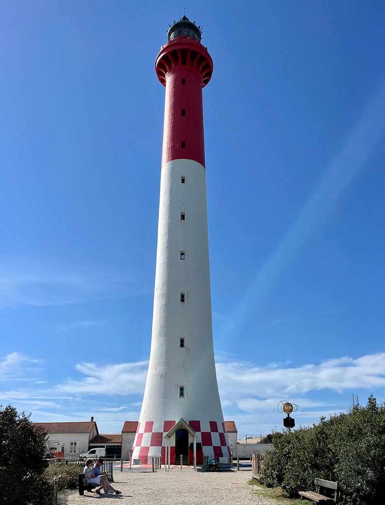 Vue de face du phare de la Coubre, rouge et blanc, se dressant sous un ciel bleu.