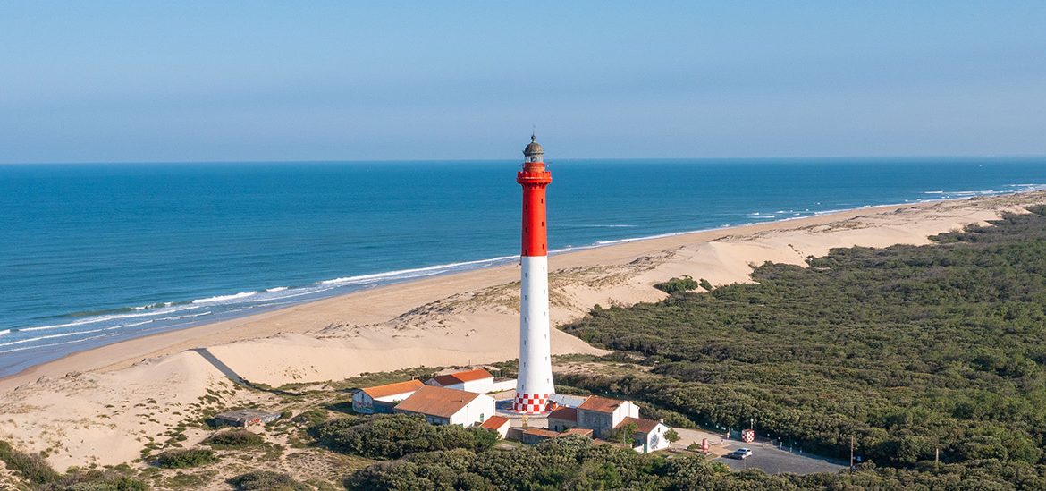 Vue aérienne du phare de la Coubre entouré de forêt dense et bordé par la plage et l’océan Atlantique.