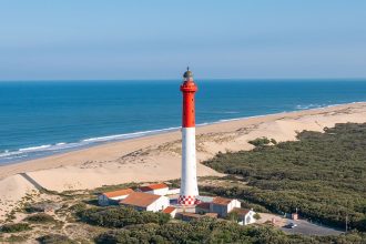 Vue aérienne du phare de la Coubre entouré de forêt dense et bordé par la plage et l’océan Atlantique.