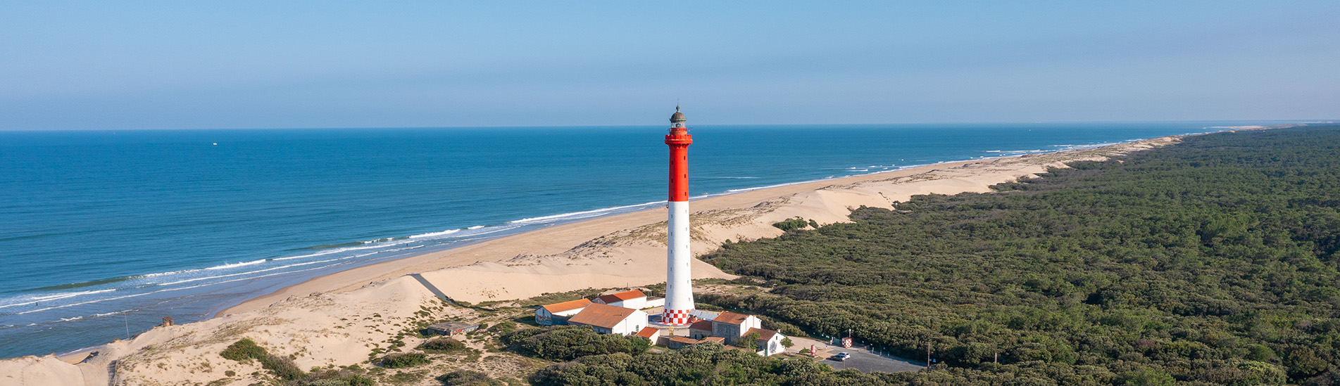 Vue aérienne du phare de la Coubre entouré de forêt dense et bordé par la plage et l’océan Atlantique.