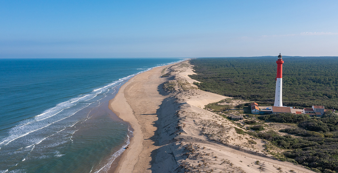 Le phare de la Coubre vu de biais depuis le ciel, surplombant une vaste plage de sable fin le long de la côte.