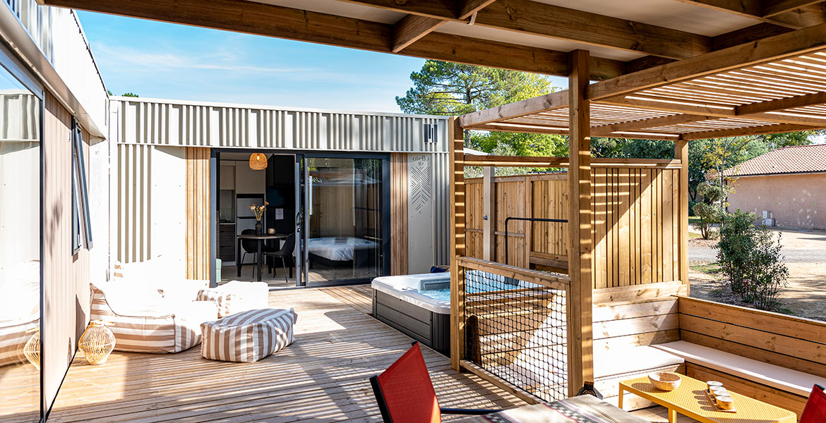 Terrasse privée d'un mobil-home haut de gamme, en bois avec jacuzzi, salon de jardin et vue sur une suite moderne.