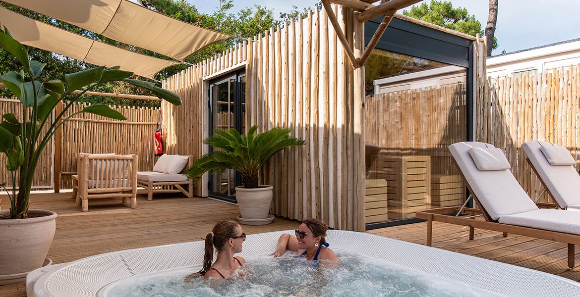 Deux femmes détendues dans un jacuzzi privatif au Camping Club La Côte Sauvage 5*, entouré de bois naturel.