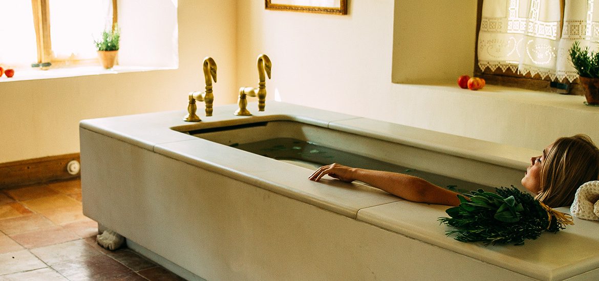 Femme allongée dans une grande baignoire de style ancien, éclairée par la lumière naturelle d’une fenêtre dans les termes d'Eugénie-les-Bains.