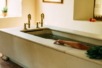 Femme allongée dans une grande baignoire de style ancien, éclairée par la lumière naturelle d’une fenêtre dans les termes d'Eugénie-les-Bains.