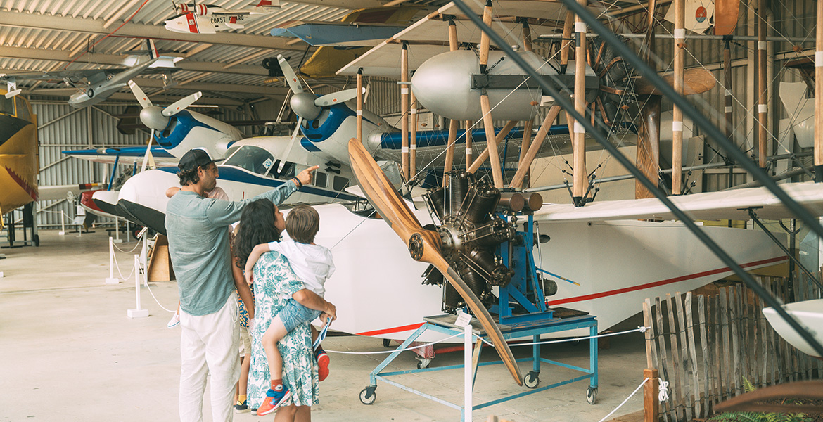 Famille observant des avions historiques et maquettes suspendues dans un hangar du musée de l'hydraviation de Biscarrosse lors d'une activités dans les Landes quand il pleut.