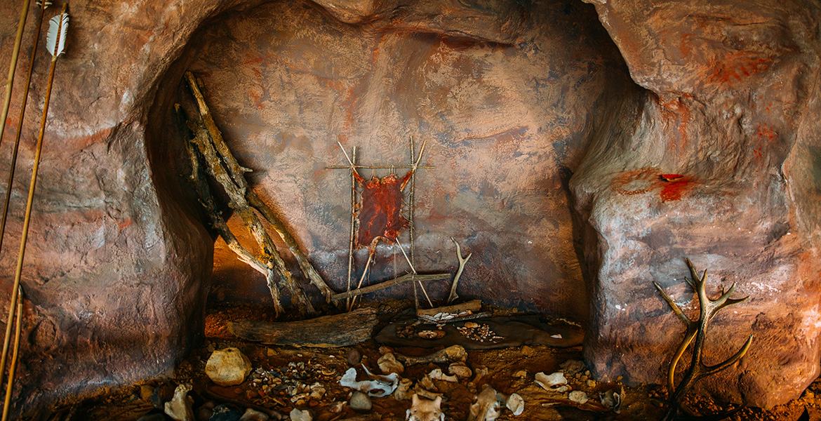Activité à faire dans les Landes quand il pleut : visiter le Préhisto'site de Brassempouy : intérieur d’une grotte avec peaux, ossements et outils exposés pour illustrer la vie des premiers hommes.
