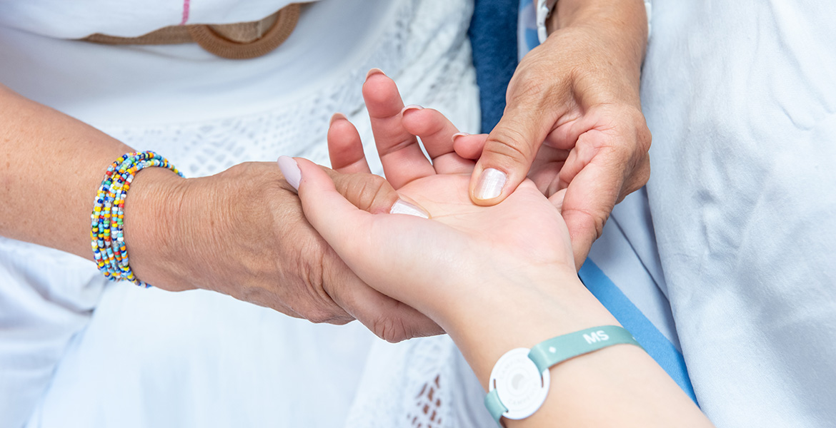 Gros plan d’un soin des mains avec pression exercée sur la paume, bracelet “MS” visible au poignet.